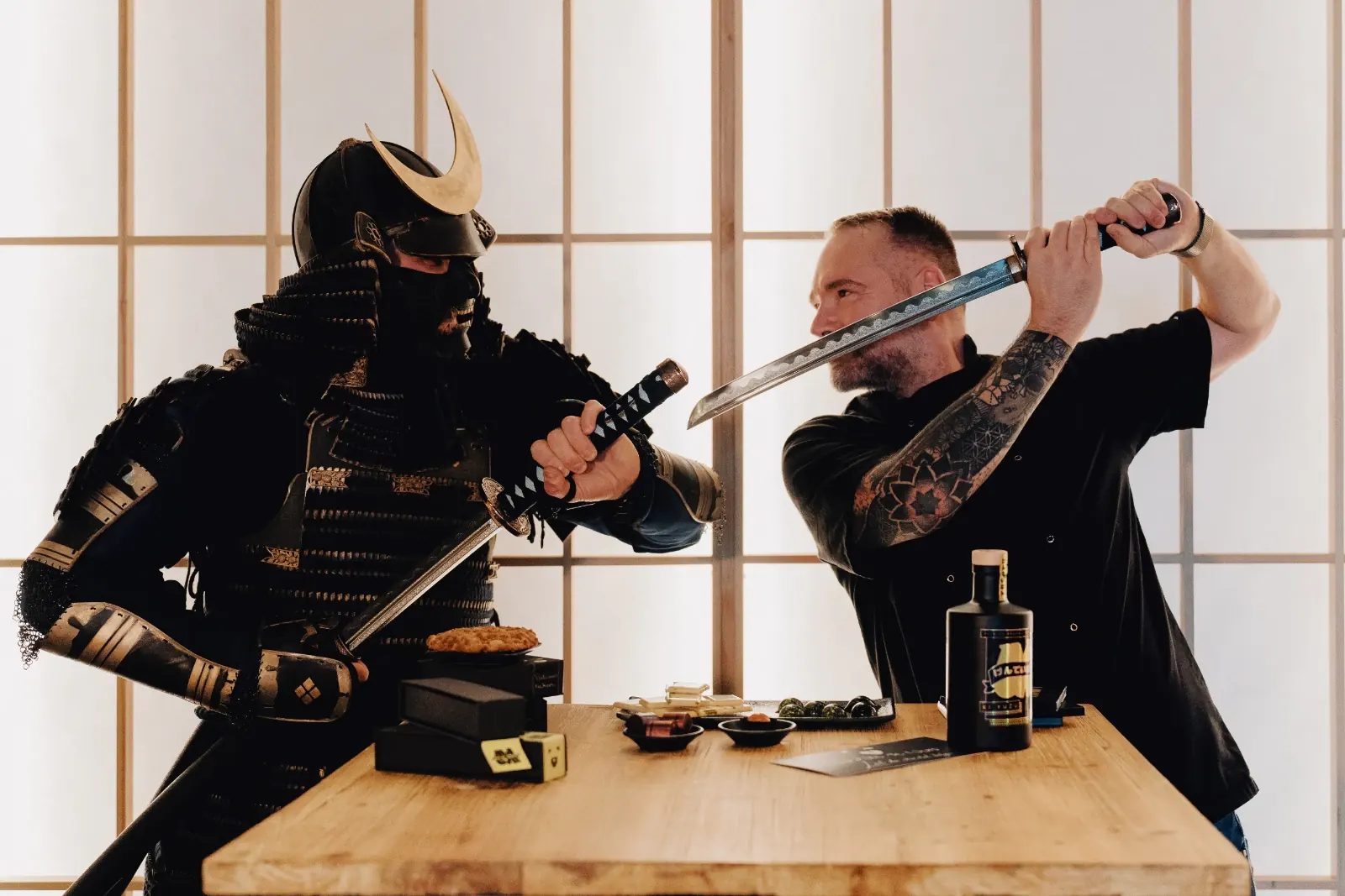 Duel de katanas entre le samouraï MaGin et un artisan, autour d'une table de chocolats et d'une bouteille MaGin