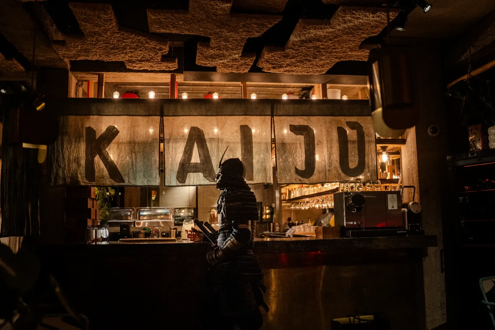 Un samouraï en armure au comptoir de Kaiju, sous le noren