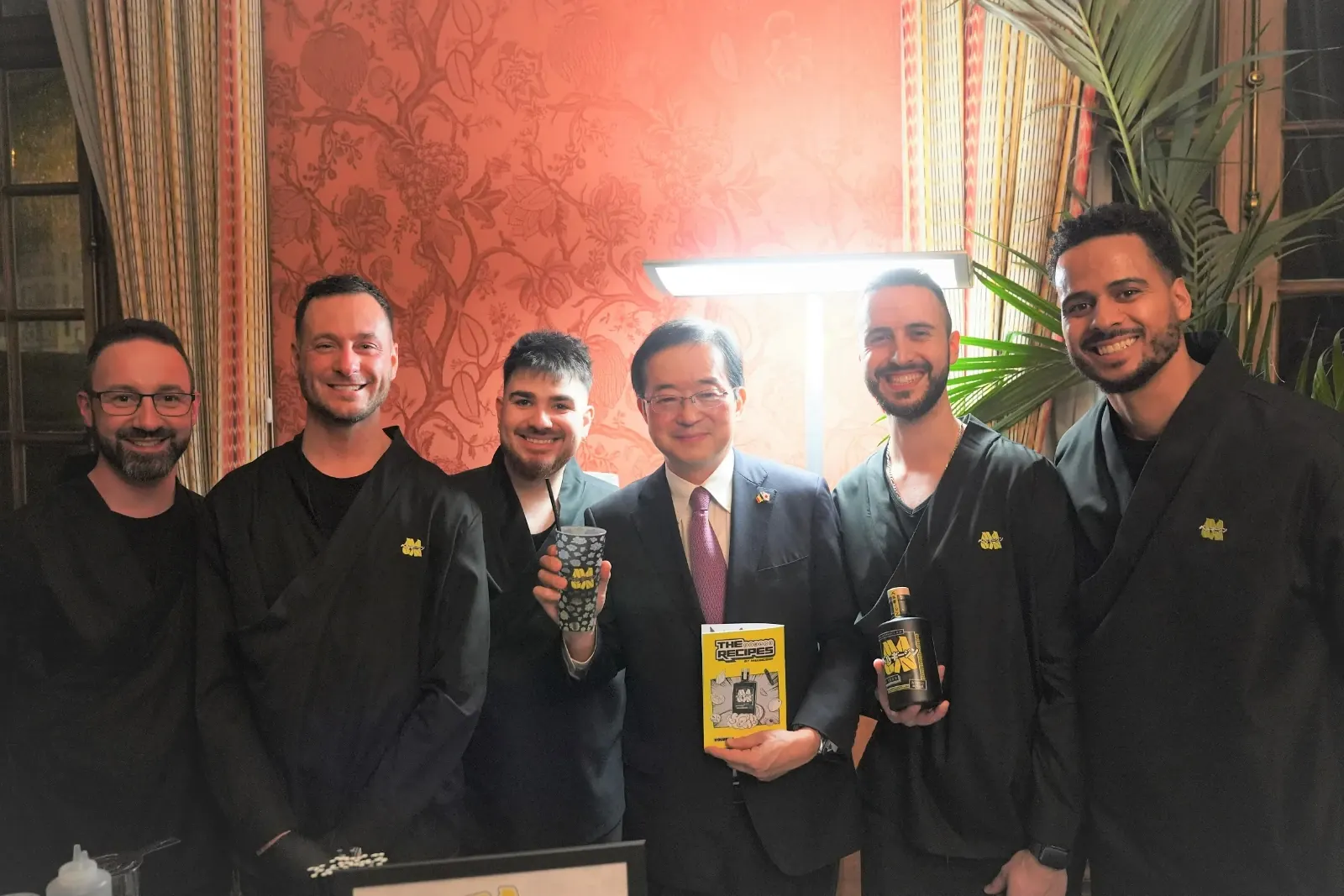The MaGin Team poses with a Japanese guest holding a MaGin cocktail and The Recipes booklet