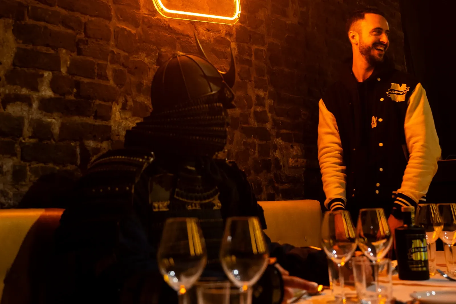 Le samouraï MaGin attablé dans un restaurant aux murs de briques, face à un membre de la Team MaGin